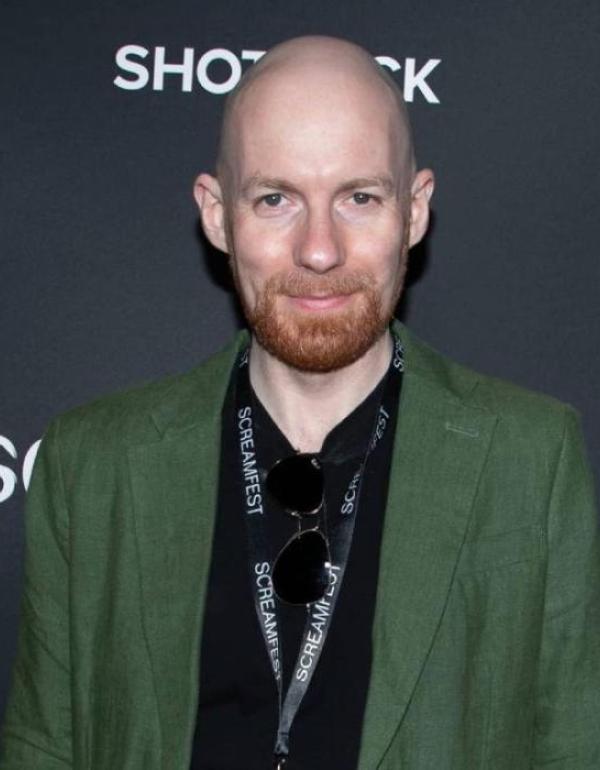 A bearded, bald man in a green suit.