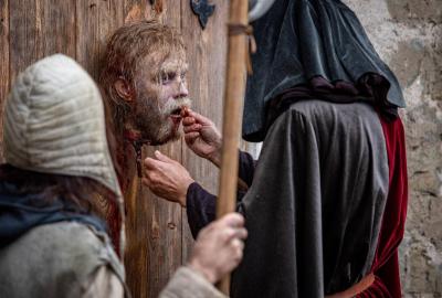 A robed man puts a coin in a decapitated head