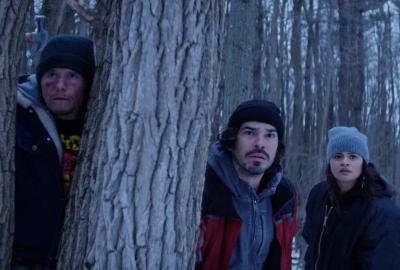 A group of guys stand amongst the trees looking on