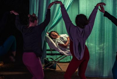 Women dance around a pregnant woman in bed