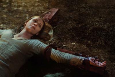 A woman is tied to a cross laying on the ground