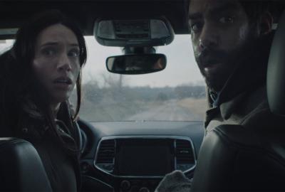 A couple look back from the front seat of a car