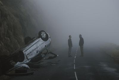 Two men talk on the road with upside down car crash