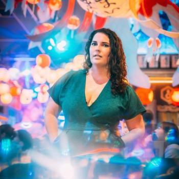 A woman in an emerald jumpsuit stands in a colorful area of the Shinjuku neighborhood of Tokyo, Japan at night