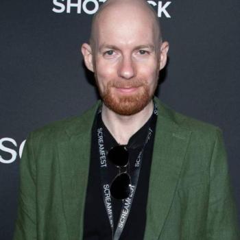 A bearded, bald man in a green suit.